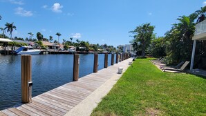 A waterfront dock with boats, a grassy walkway, and palm trees. - Relax & Unwind – Walk to the Beach from This 2BR -2BA with Pool and fishing dock (Pompano Beach)