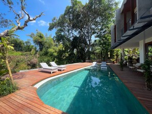 A swimming pool with wooden deck and lounge chairs, surrounded by lush greenery and trees. - Leafy Riverbank (Tabanan)