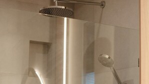 Une salle de bain moderne dotée d’une douche à parois de verre, d’une fenêtre visible et d’un miroir encastré.