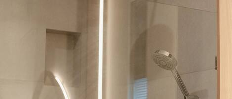Une salle de bain moderne dotée d’une douche à parois de verre, d’une fenêtre visible et d’un miroir encastré.