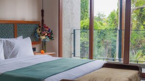 Une chambre d’hôtel avec un grand lit, une table de chevet ornée d’un vase de fleurs et une vue sur la verdure grâce à de grandes fenêtres.