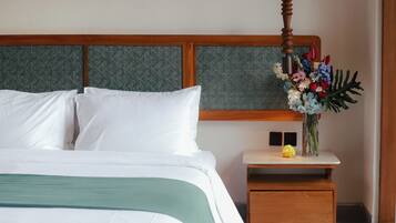A neatly made bed with white linens, a wooden headboard, a bedside table with a vase of flowers, and a small wooden nightstand.