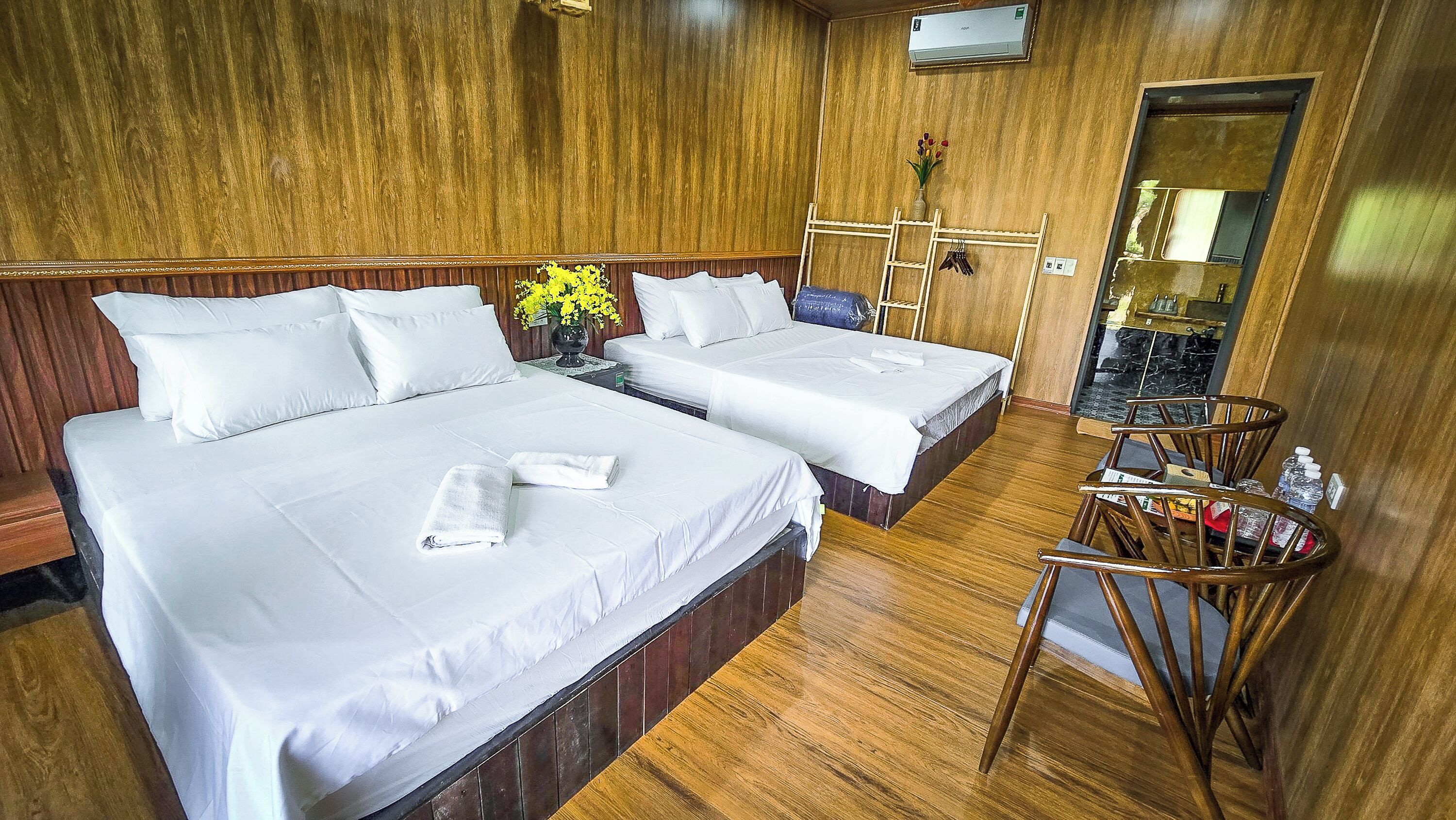 A hotel room with two beds, wooden walls, a small table with a vase of flowers, and a mirror.