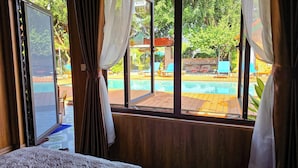 A room with a large window overlooking a pool area, wooden flooring, and a bed with a patterned bedspread. - Tam Coc Holiday Retreat (Nam Hoa Lu)