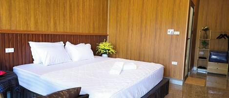 A hotel room with a large bed, wooden paneling on the walls, a small table with a vase of flowers, and a wardrobe with hanging clothes.