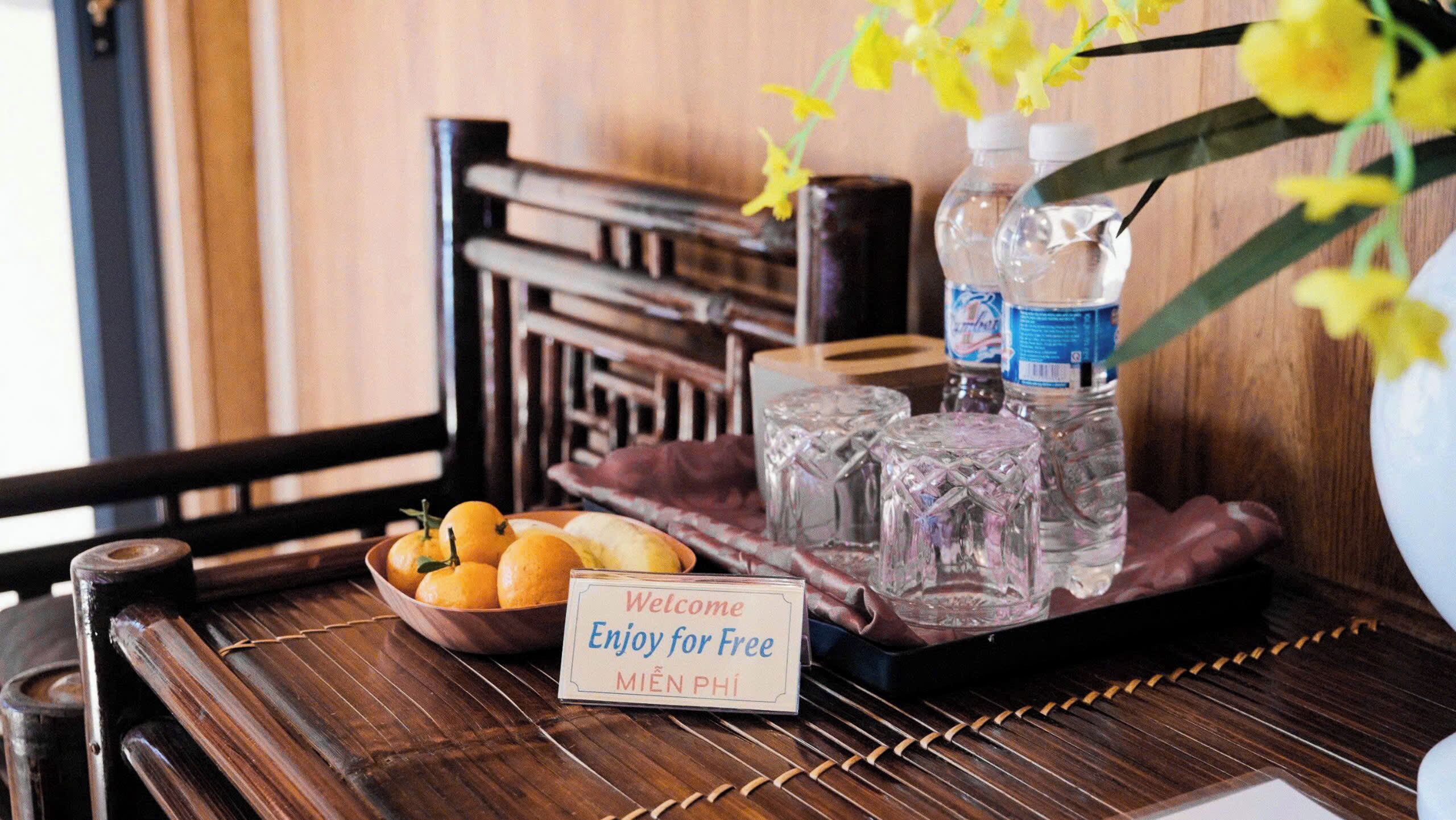A wooden table with a bowl of oranges, two bottles of water, and a sign that says "Welcome Enjoy for Free MIEN PHI".