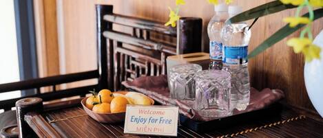 A wooden table with a bowl of oranges, two bottles of water, and a sign that says "Welcome Enjoy for Free MIEN PHI".