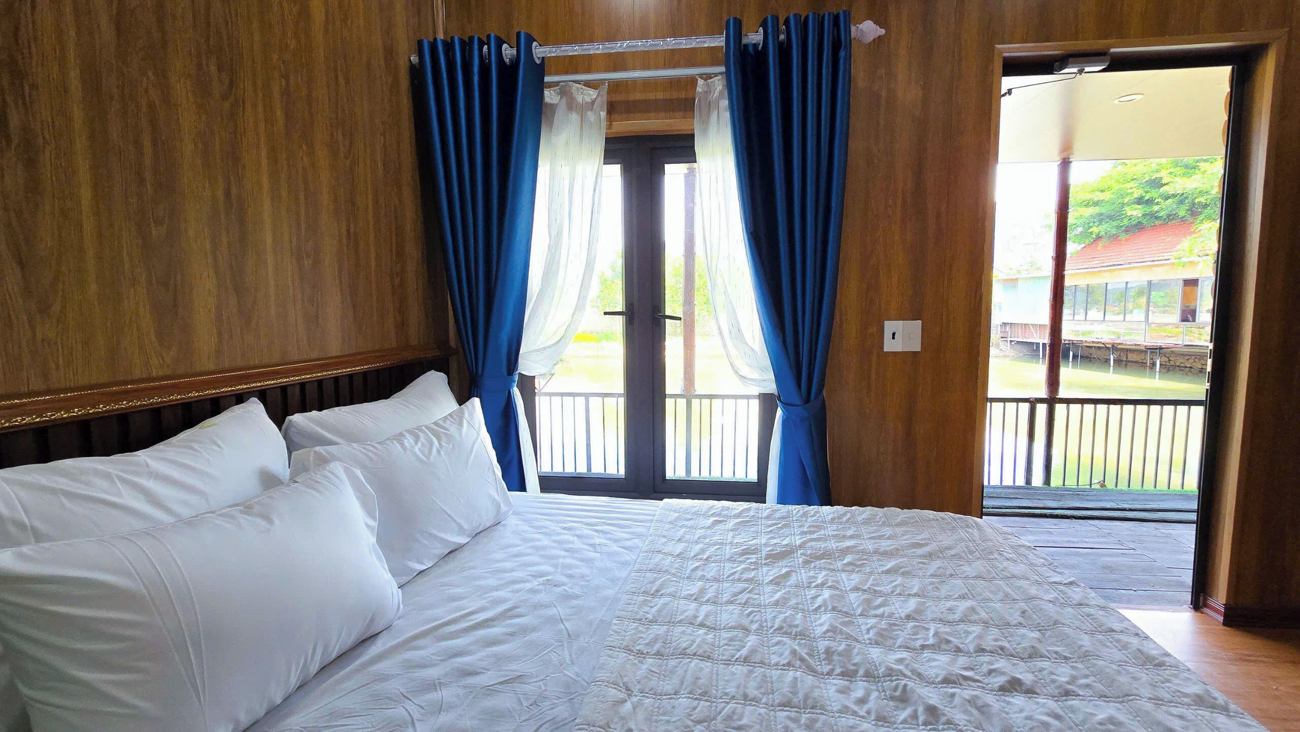 A bedroom with a large bed, wooden walls, and a balcony with blue curtains.