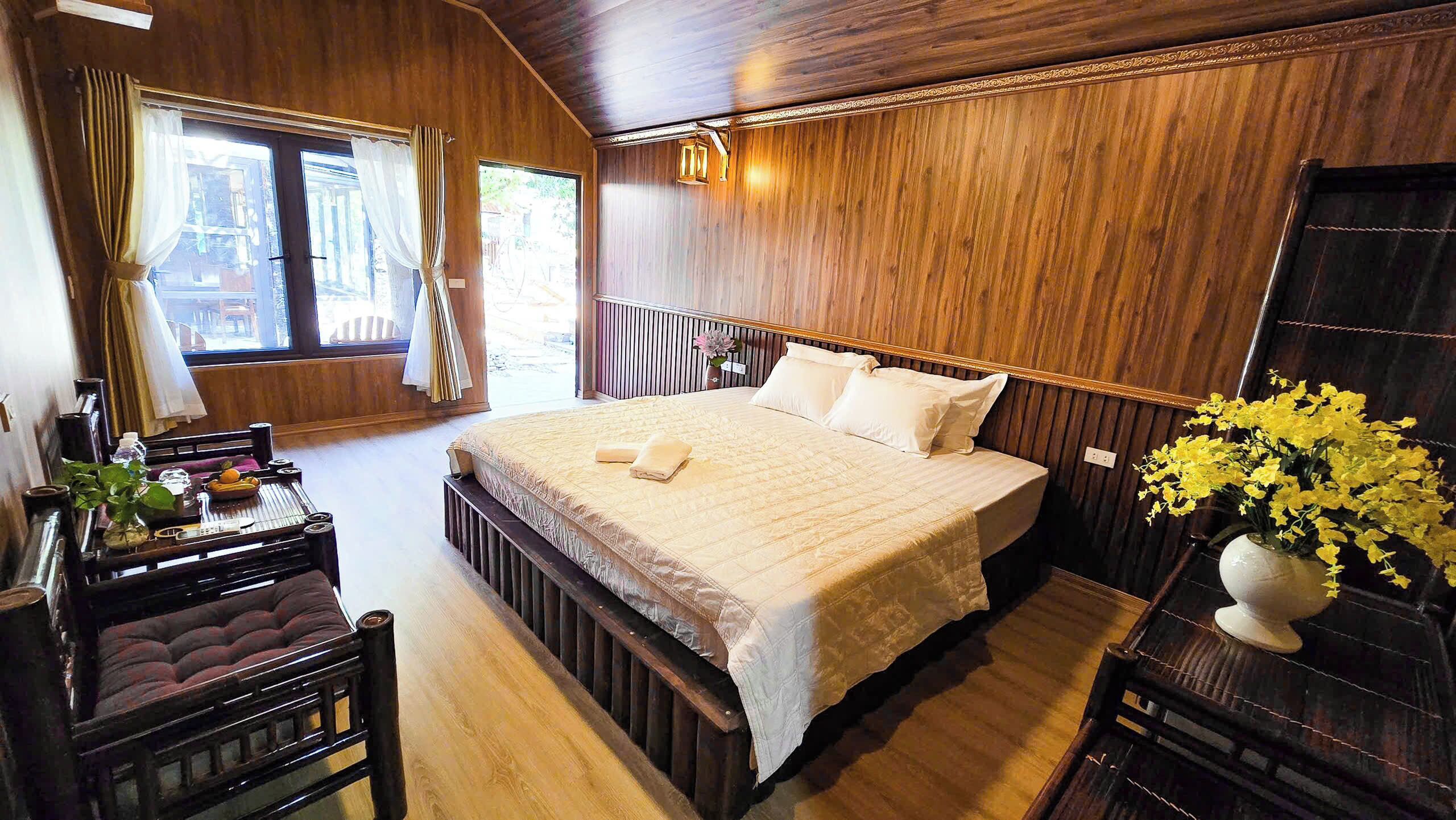 A wooden-paneled bedroom with a bed, bedside table, chair, and a vase of flowers.