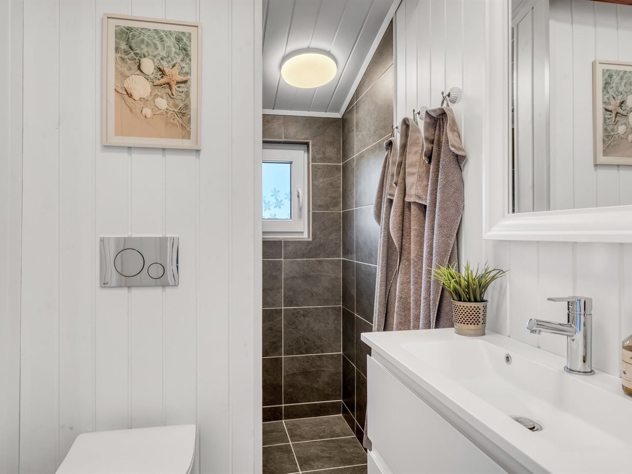 A bathroom with a white vanity, a shower with dark tiles, and a framed picture on the wall.