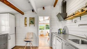 A modern kitchen with white cabinetry, a wooden ceiling, and a view to the dining area.