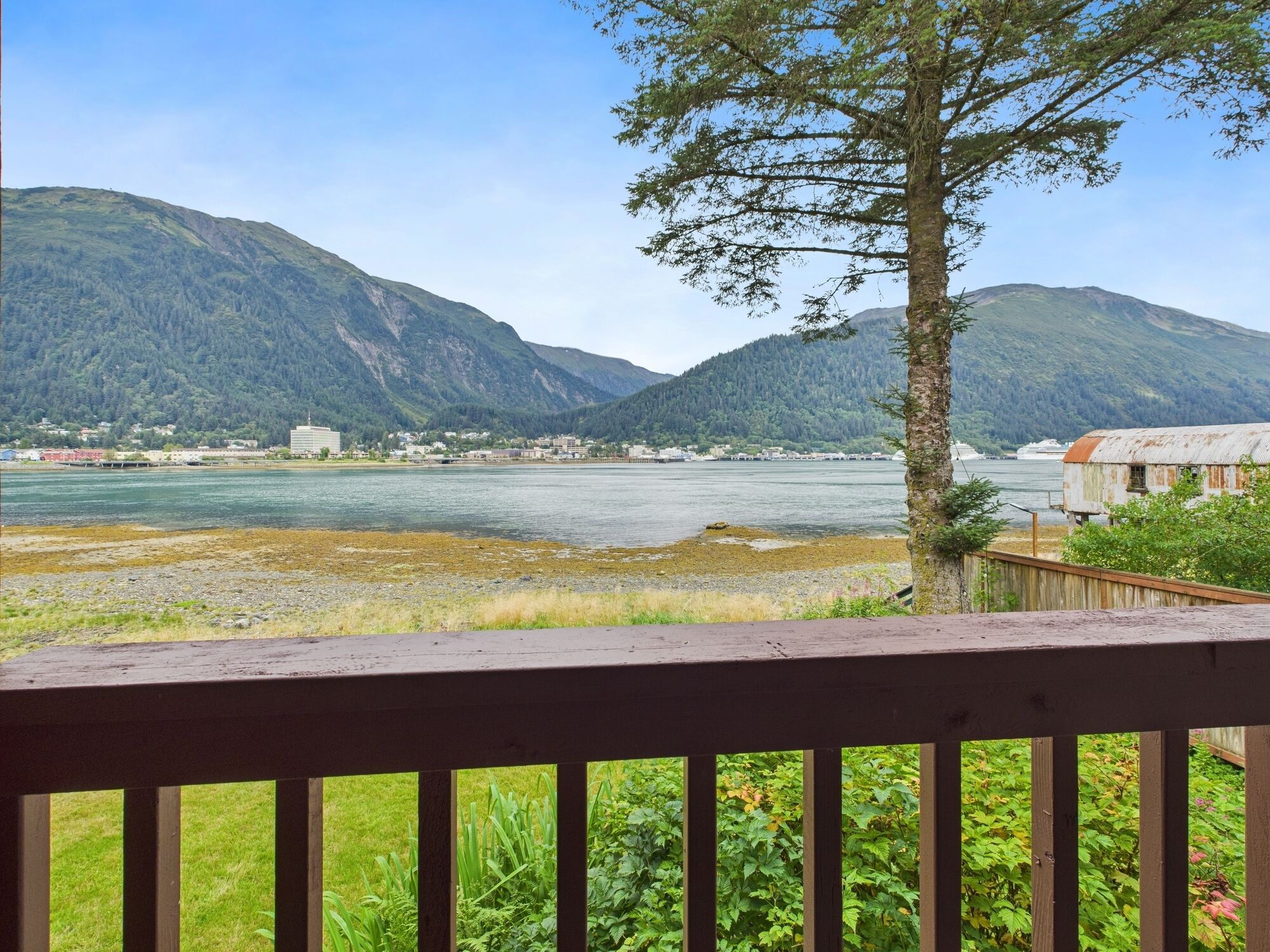 A view of a river with mountains in the background, a wooden deck in the foreground, and a small building on the right.