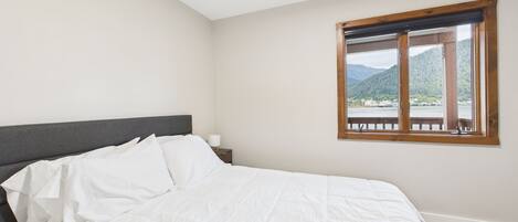 Una camera da letto con un letto, un comodino e una finestra vista lago e montagne.