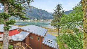 A cabin with a metal roof, wooden deck, and a view of a lake and mountains. - Oceanfront w/ Incredible Views (Juneau)