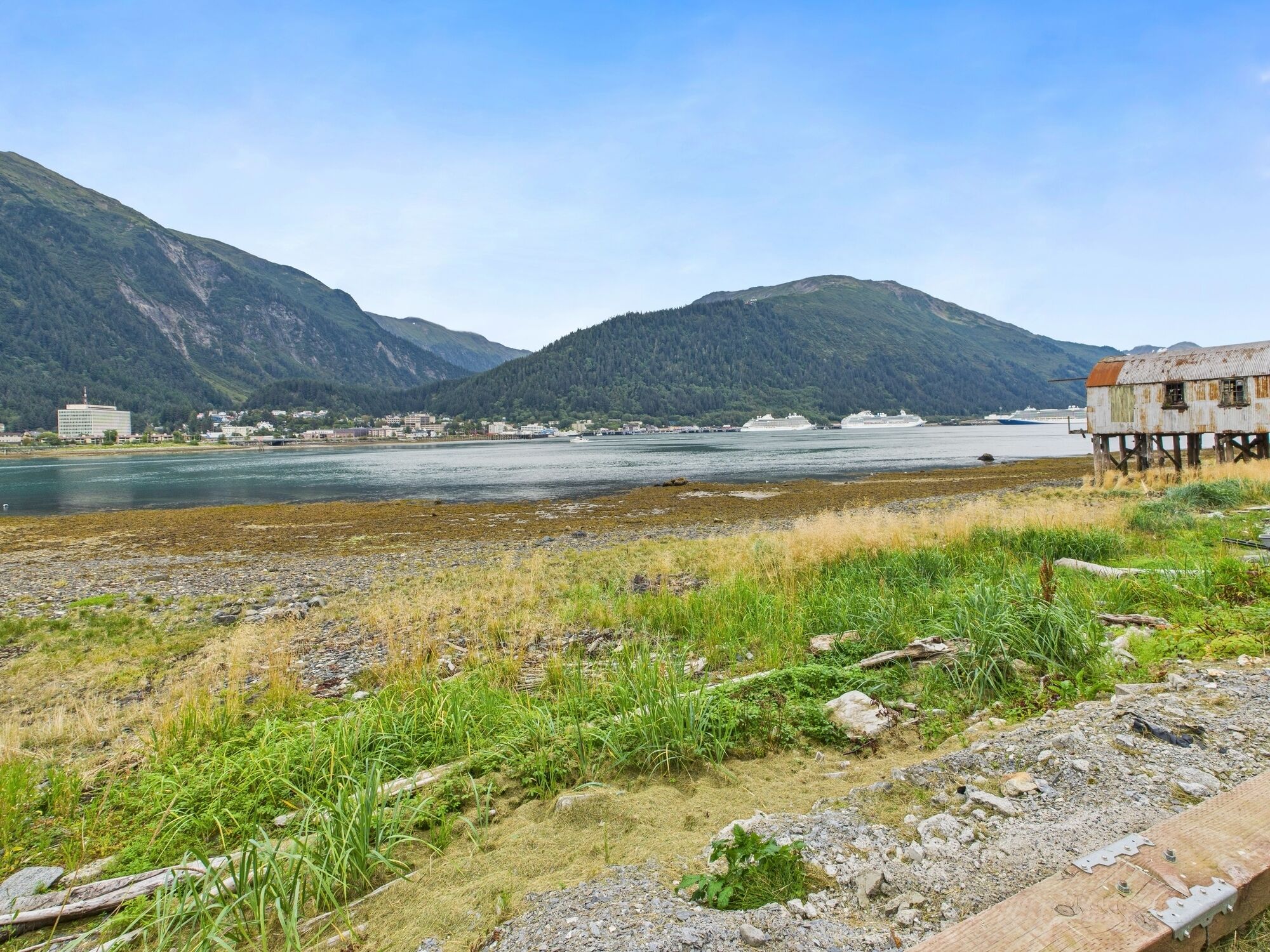 A riverside view with mountains, a wooden structure, and buildings in the background.