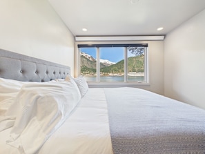 Ein Schlafzimmer mit einem großen Bett, Blick auf einen See und Berge, und einem modernen Deckenstil.