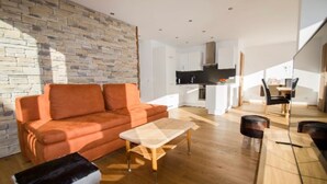 En moderne stue med en stenvæg, en sofa, et sofabord og et spiseområde med stole og et bord.
