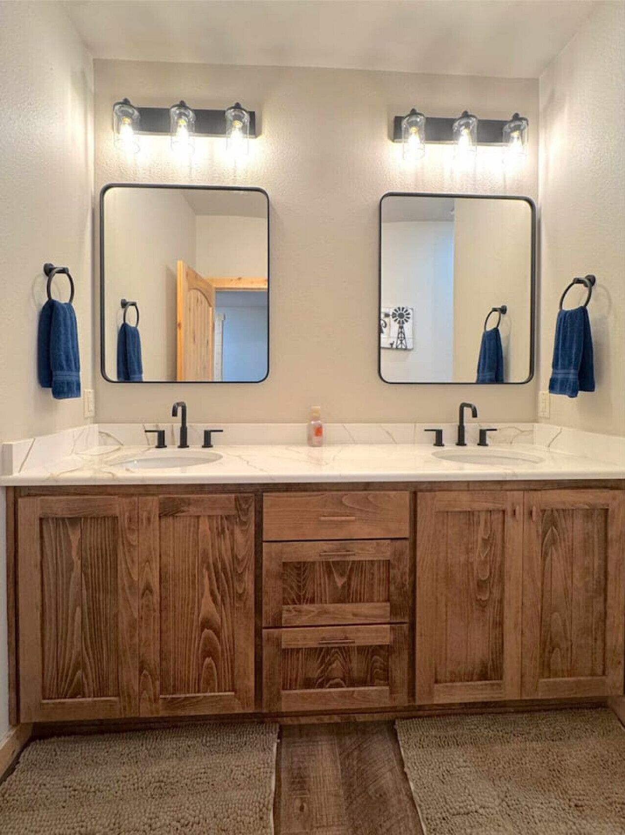 Un baño con dos lavamanos, armarios de madera y un espejo grande con iluminación superior.