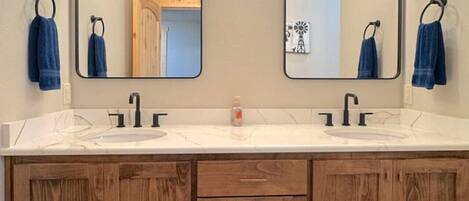 Un baño con dos lavamanos, armarios de madera y un espejo grande con iluminación superior.