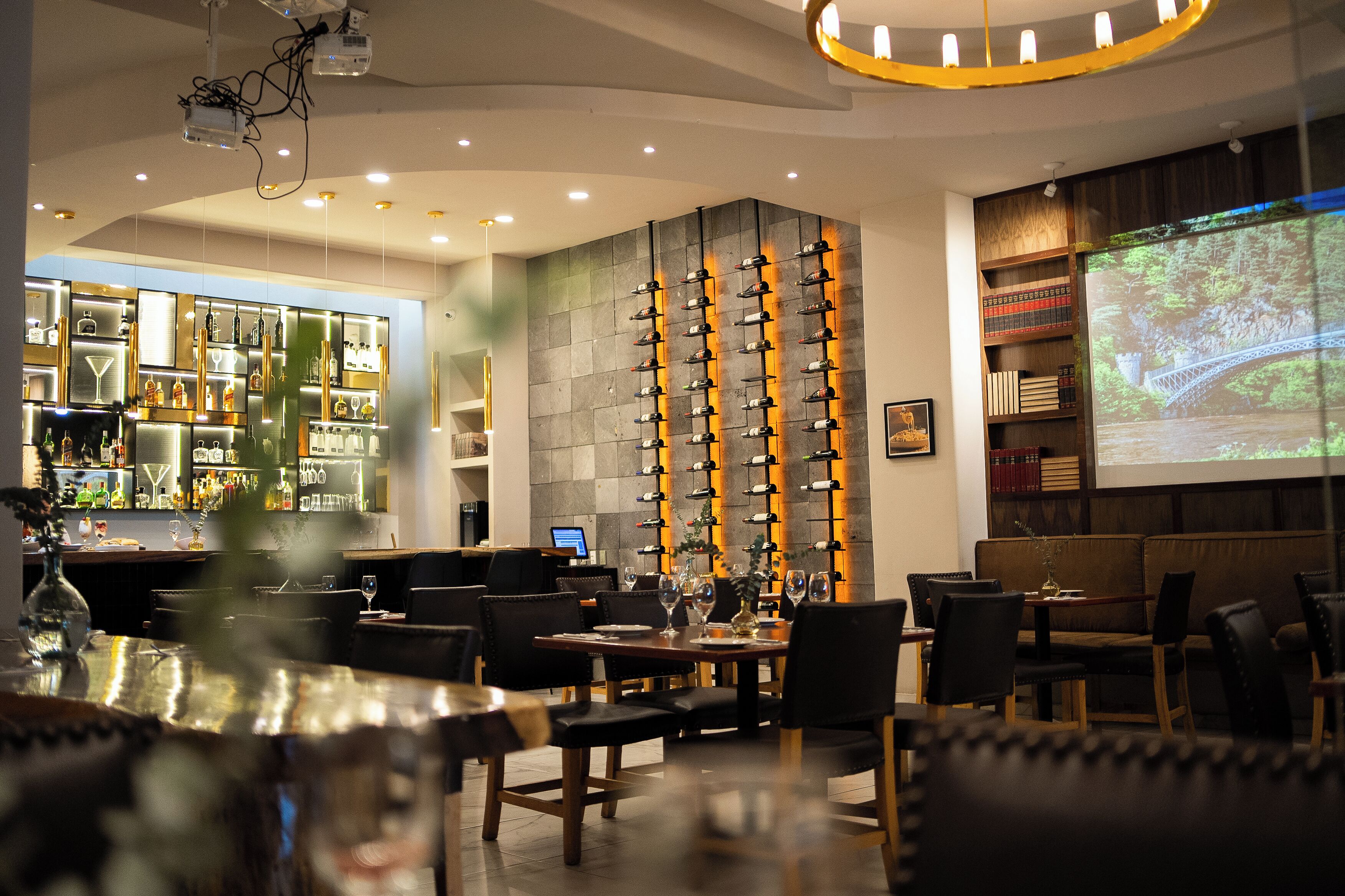 A bar area with a wine rack, seating, and a projection screen displaying a scenic image.