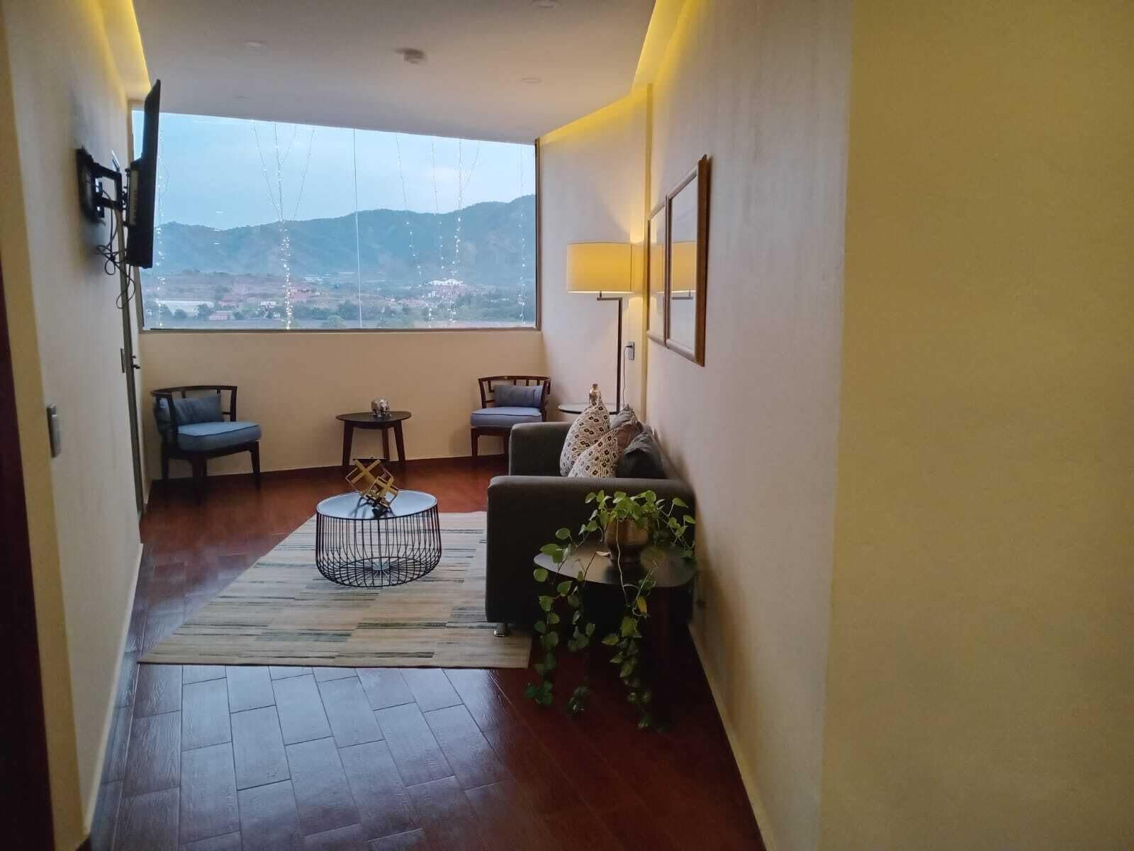 Ein modernes Wohnzimmer mit großem Fenster, einer Couch, zwei Sesseln, einem Couchtisch und einer Stehlampe.