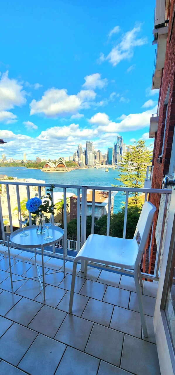A balcony with a view of a city skyline, a table with a vase of flowers, and a chair.