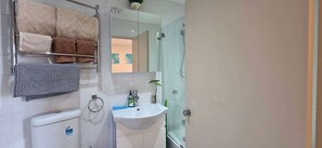 Un bagno con cabina doccia in vetro, un lavandino bianco e un portasciugamani con diversi asciugamani.