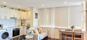 A compact living space with a kitchenette, a sofa, a dining table, and a window with curtains.