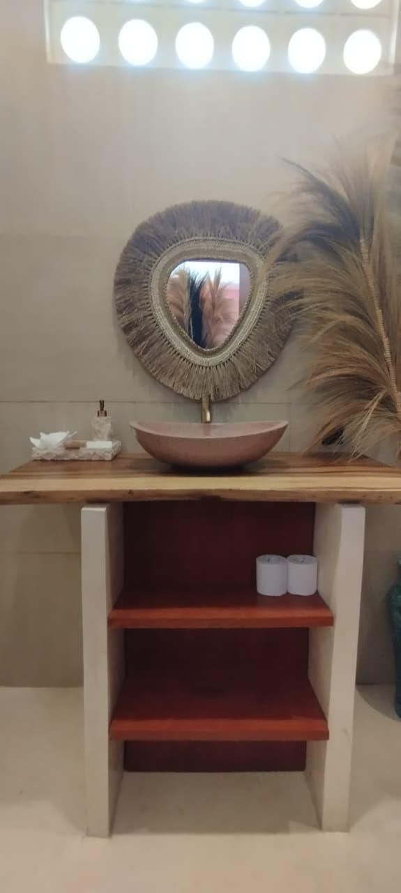 Un tocador de baño con un espejo redondo, un lavabo rosa y un estante con dos rollos de papel higiénico.