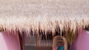 Un área de piscina con techo de paja, una silla de mimbre y una planta en maceta.