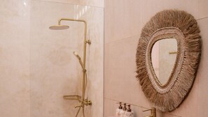 Un baño con tocador de madera, un espejo redondo con flecos y una ducha independiente con accesorios dorados.