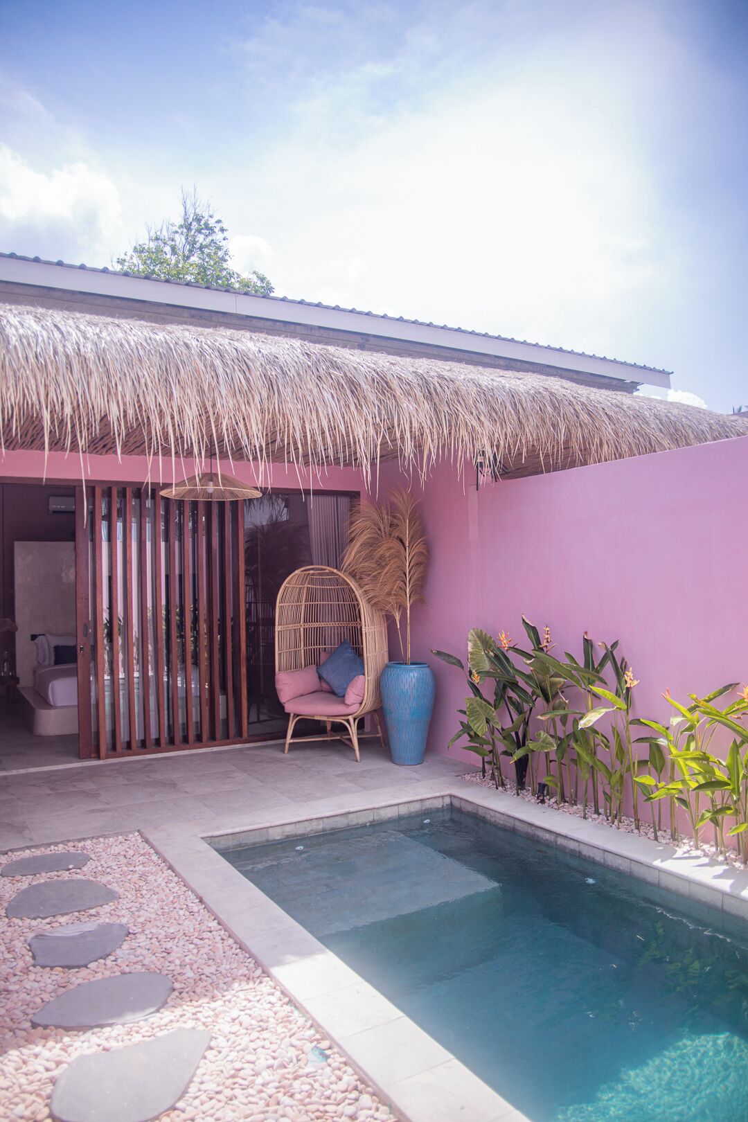 Un área de piscina con techo de paja, una silla de mimbre y plantas tropicales.