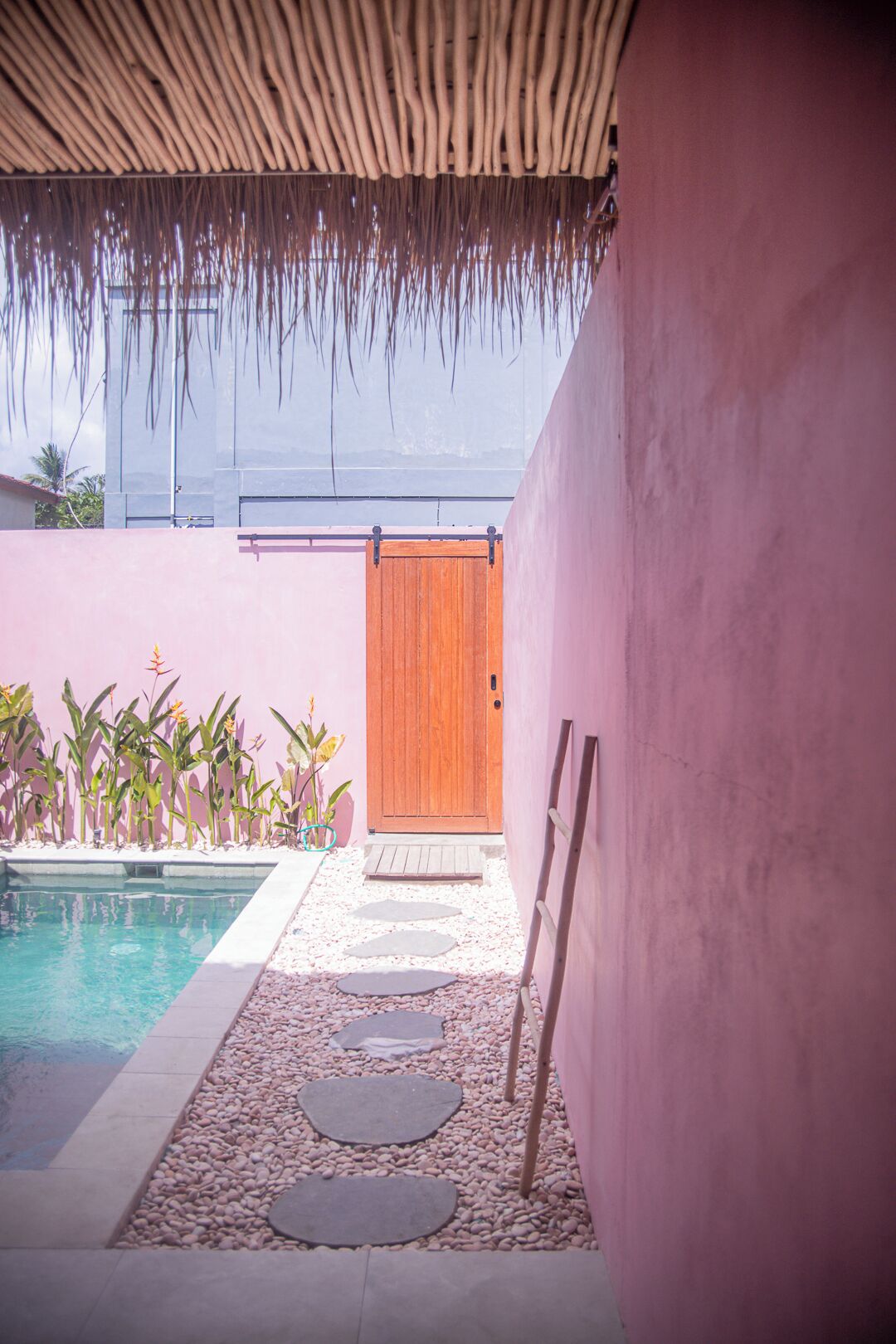 A pool area with a wooden door, pebbles, and a thatched roof.