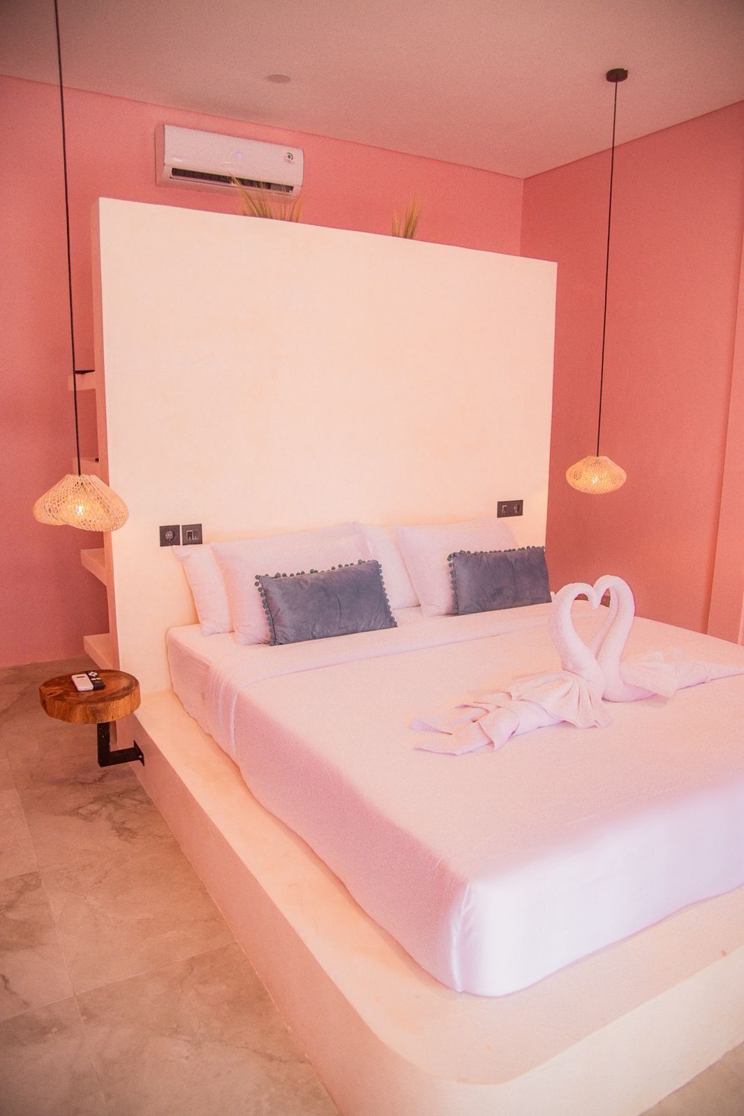A bedroom with a large bed, two bedside lamps, a bedside table, and a wall-mounted air conditioner.