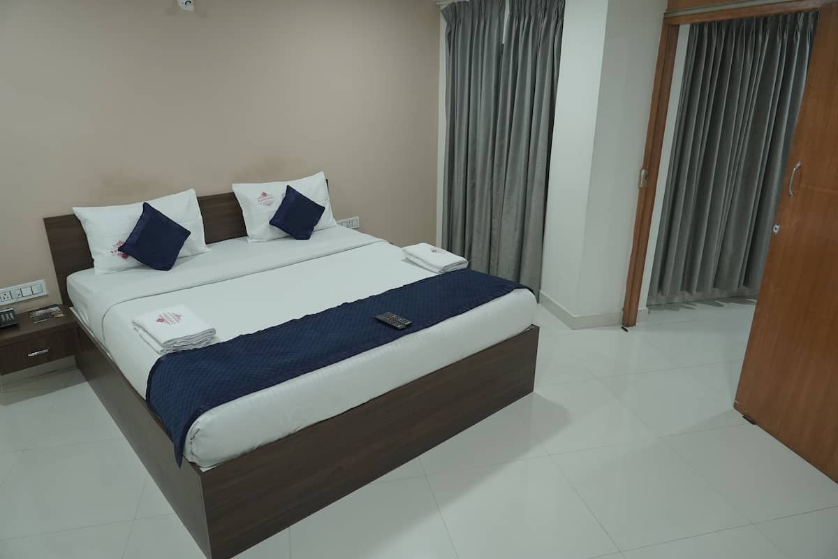 Cama bem arrumada com manta e almofadas azuis, mesa de cabeceira com telefone e toalha dobrada, e guarda-roupa de madeira.