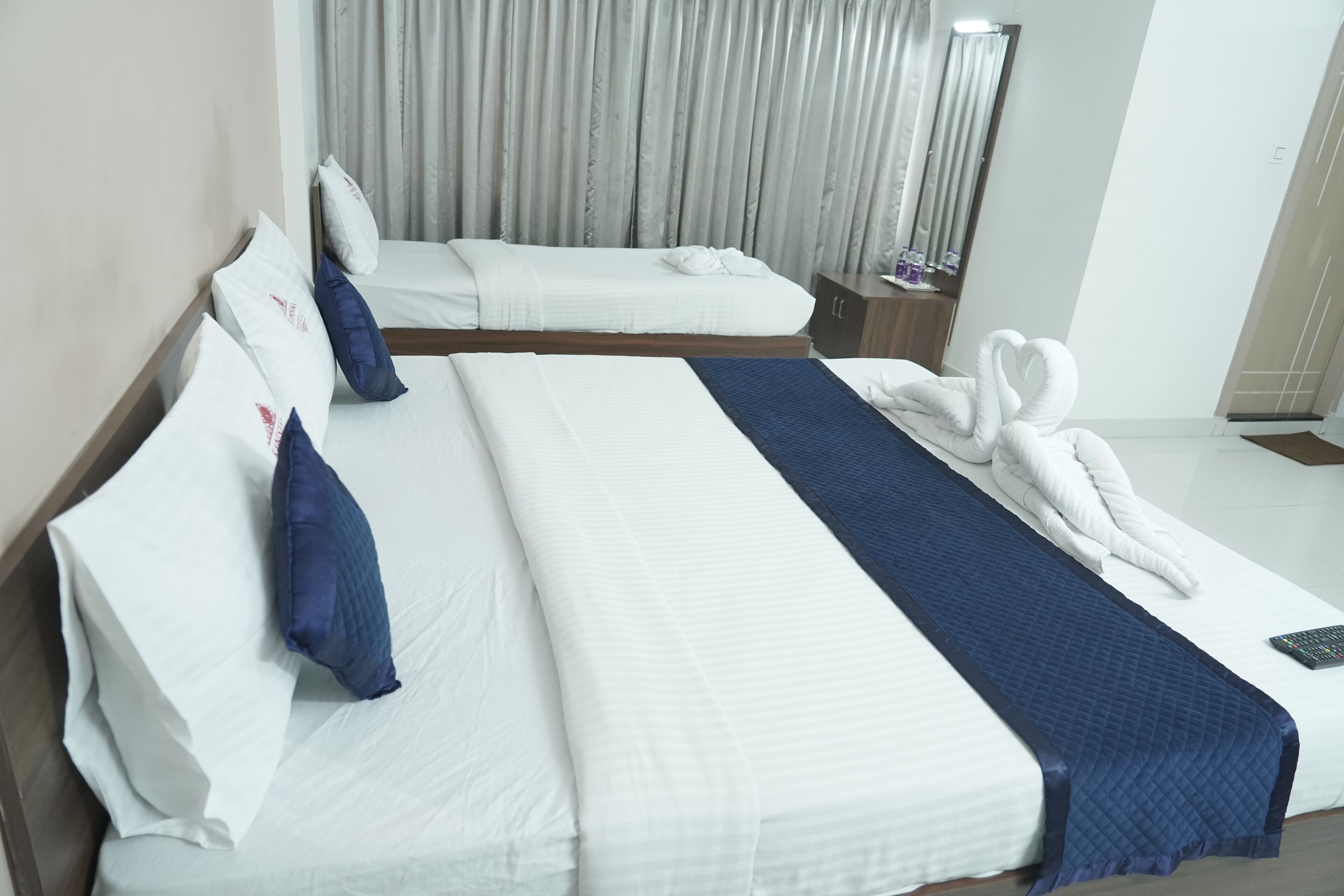 A hotel room with two beds, a blue quilted bed runner, white linens, and a towel arrangement.
