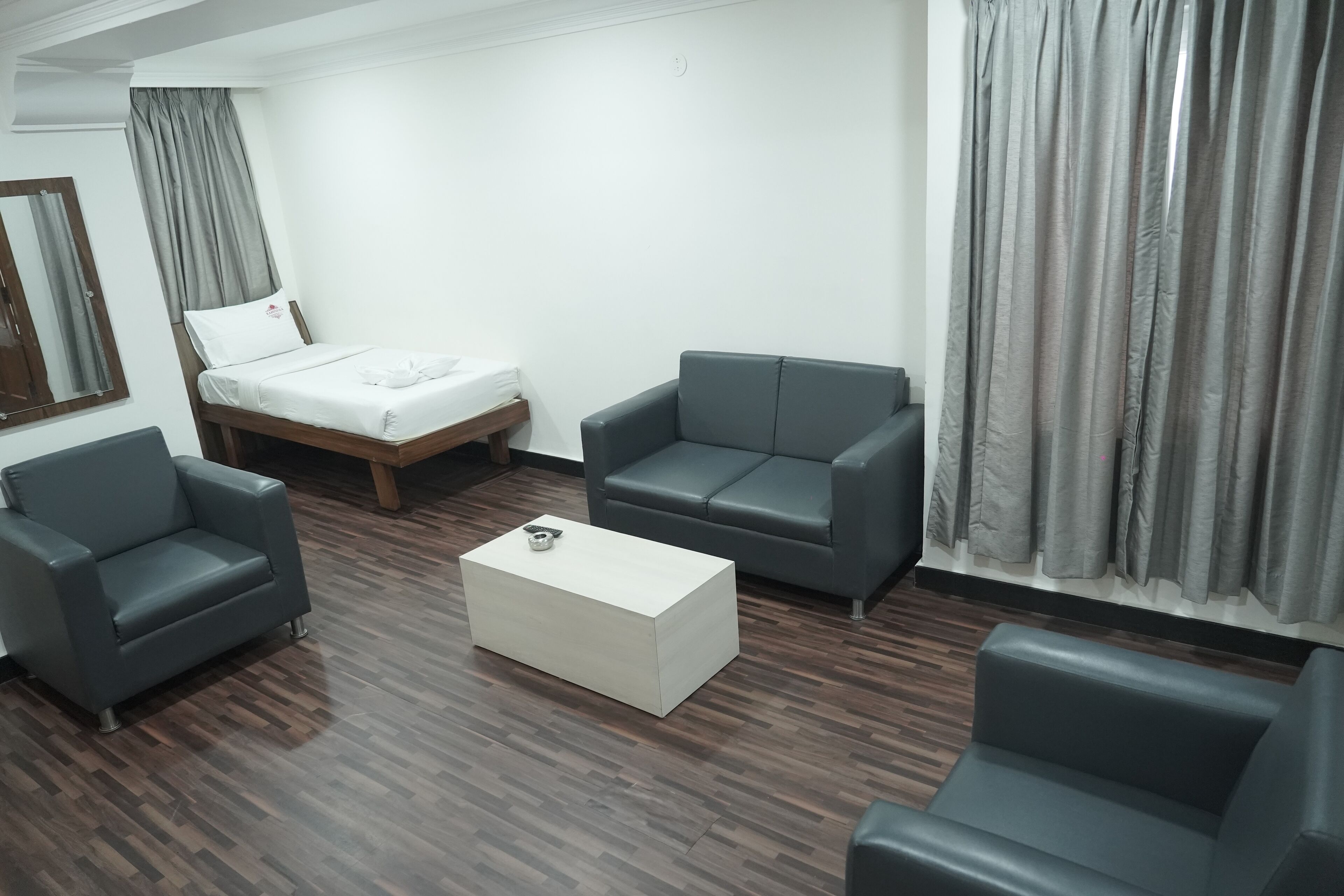 Une chambre d’hôtel moderne avec un lit, deux canapés, une table basse et un plancher en bois.