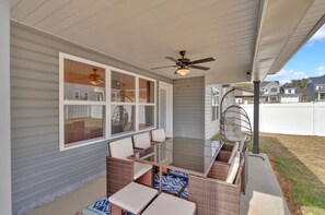 A covered patio with wicker furniture, a ceiling fan, and large windows.