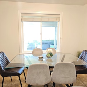 Un coin repas avec une table en verre, quatre chaises et une fenêtre équipée de stores.