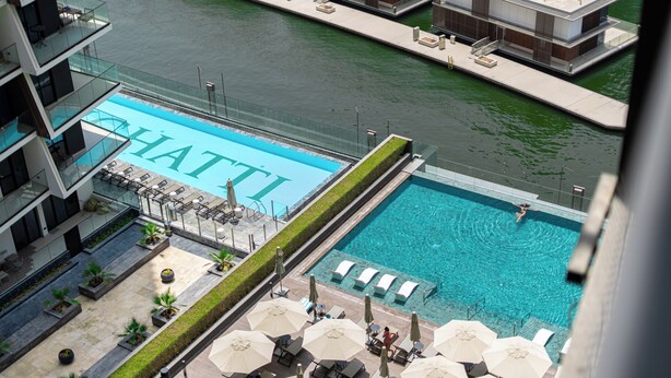 Une piscine sur le toit offrant une vue dégagée sur l’eau, entourée de chaises longues et de parasols.