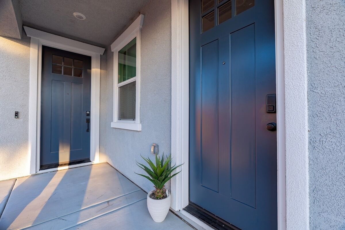 A house entrance with two blue doors, a white potted plant, and a small window.