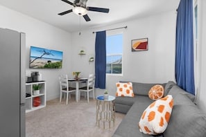 A modern living room with a grey sofa, a dining table with chairs, a ceiling fan, and artwork on the walls.