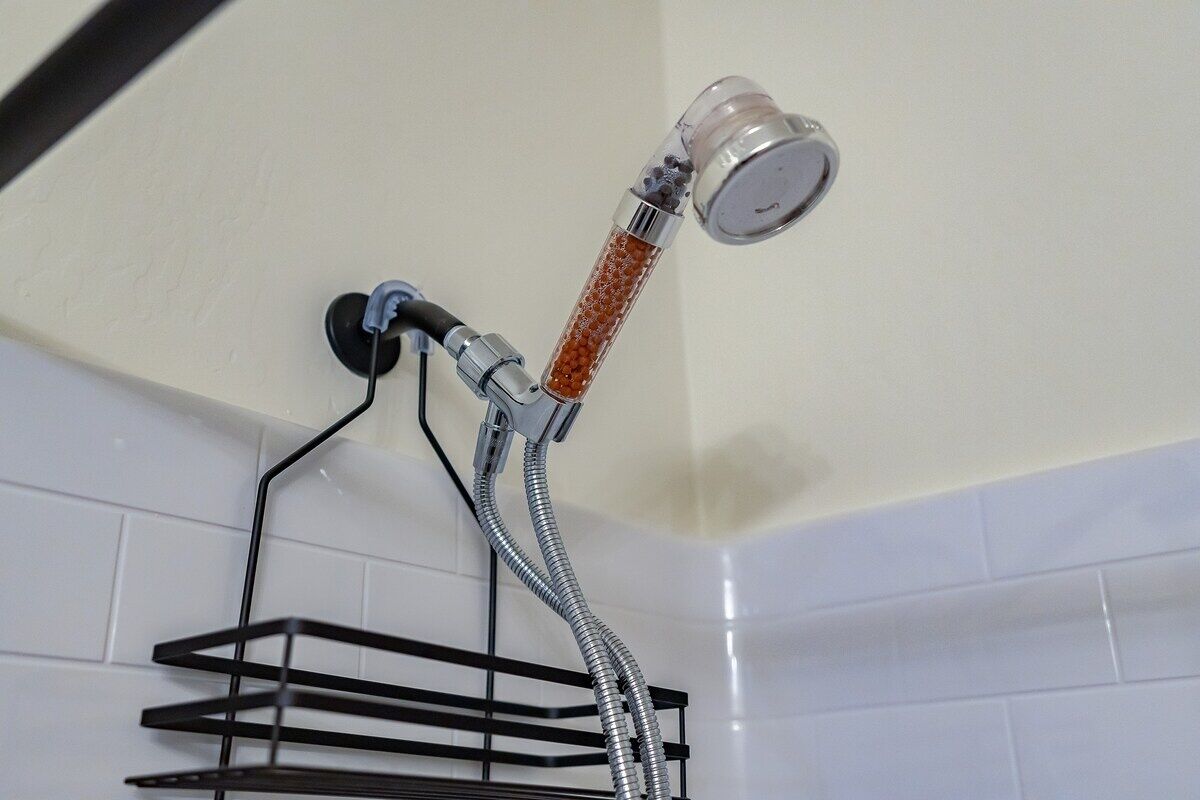 A shower with a flexible hose and a transparent container with red beads.