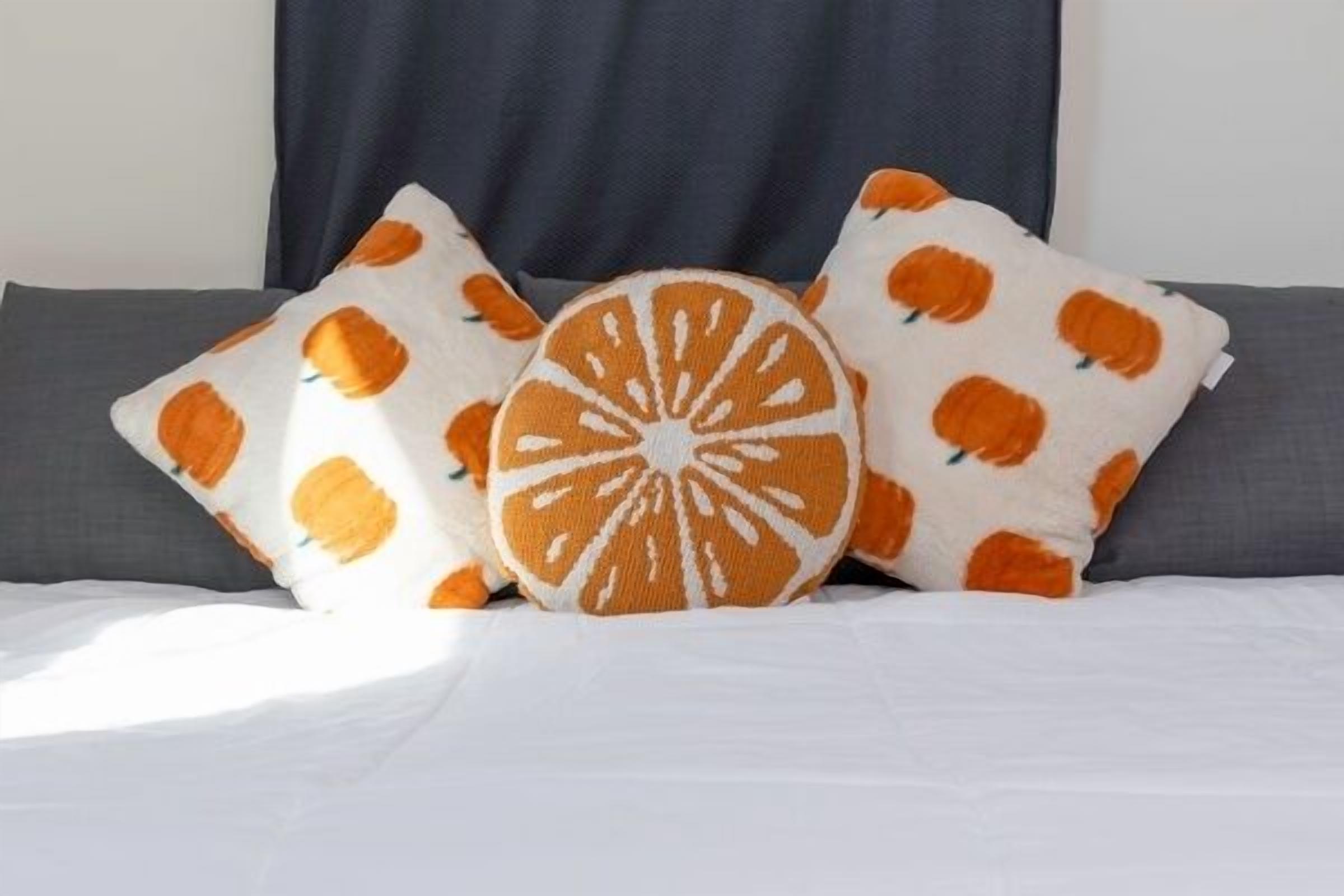 A bed with white bedding and three pillows with orange and white patterns.