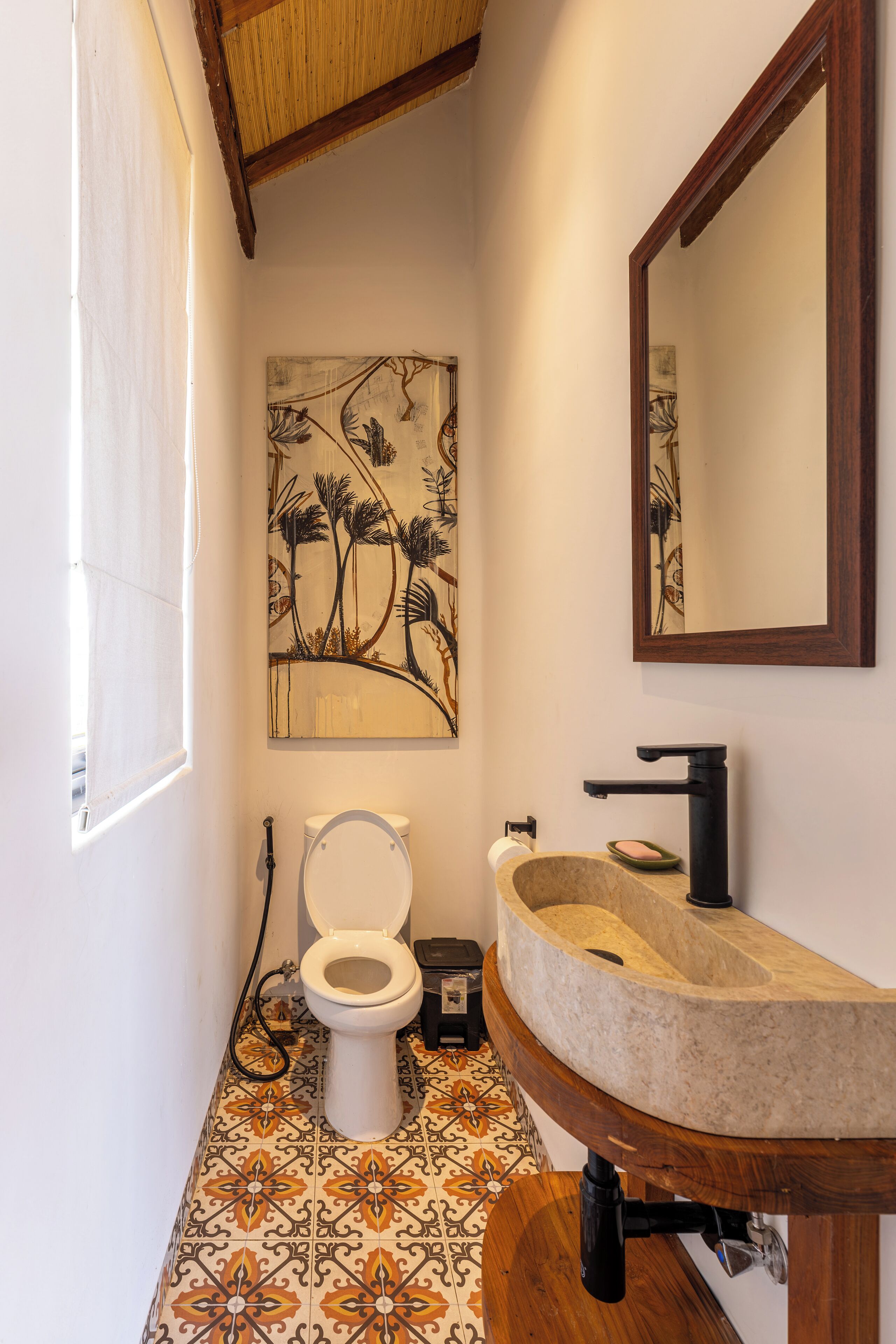 A bathroom with a toilet, sink, and a painting on the wall.
