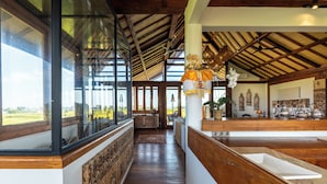 Un intérieur spacieux avec de hauts plafonds, des poutres en bois et de grandes fenêtres offrant une vue sur l’extérieur.
