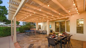 Une terrasse extérieure avec une table et des chaises, une table de ping-pong et des guirlandes lumineuses.