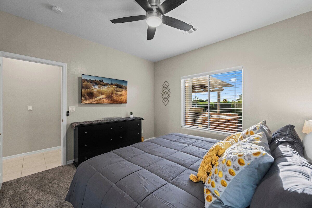 Ein Schlafzimmer mit einem großen Bett, einem Deckenventilator, einem Schminktisch, einem Gemälde und einem Fenster mit Jalousien.