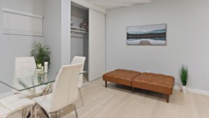 A modern living room with a glass dining table, white chairs, a brown leather sofa, a white armchair, and a potted plant. - Relax & Unwind - Cozy 1 BR w/ Room for 5 Guests (San Diego)