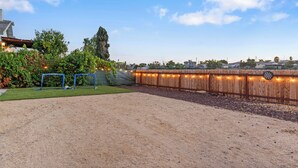 A fenced backyard with a dirt area, a blue play structure, and a wooden fence with string lights. - Relax & Unwind - Cozy 1 BR w/ Room for 5 Guests (San Diego)